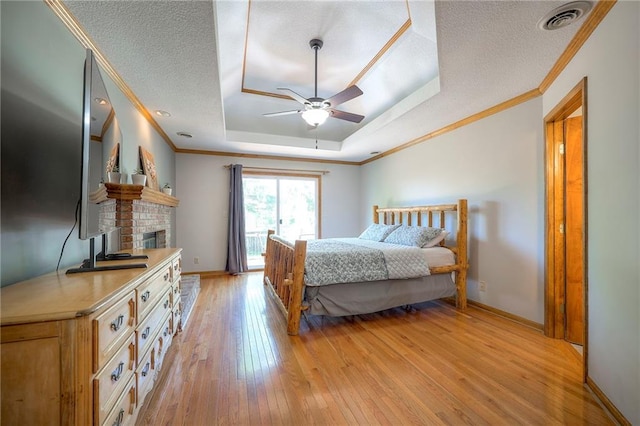 1906 Blackbird Cir, Kearney, MO 64060 - bedroom with a tray ceiling, light wood-style flooring, crown molding, a brick fireplace, and a textured ceiling