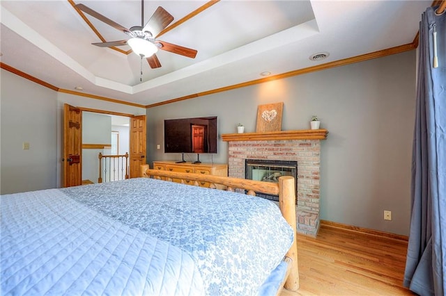 1906 Blackbird Cir, Kearney, MO 64060 - bedroom featuring a raised ceiling, light wood-style flooring, ornamental molding, a brick fireplace, and ceiling fan