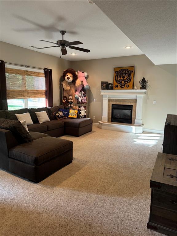 carpeted living area with ceiling fan, a tile fireplace, baseboards, and recessed lighting