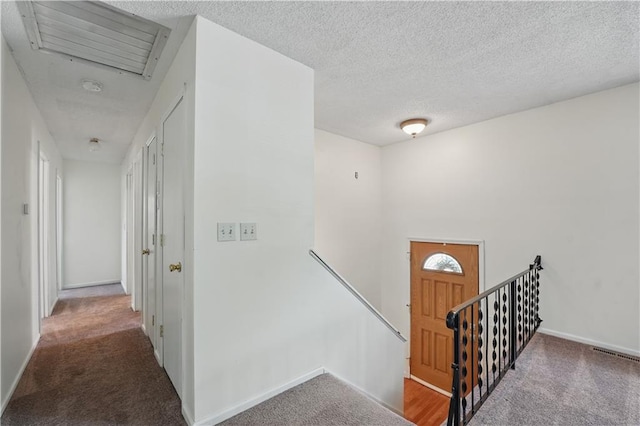 hall featuring an upstairs landing, carpet floors, baseboards, and a textured ceiling