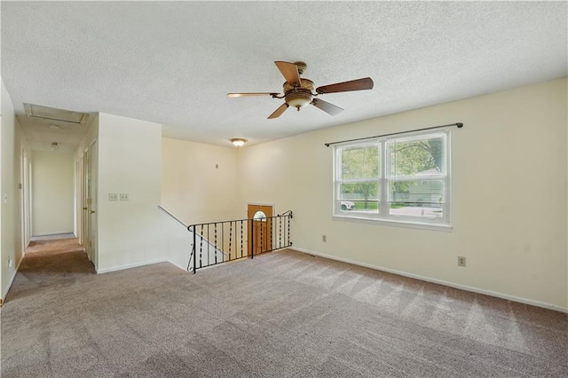 unfurnished room with carpet, a ceiling fan, attic access, a textured ceiling, and baseboards
