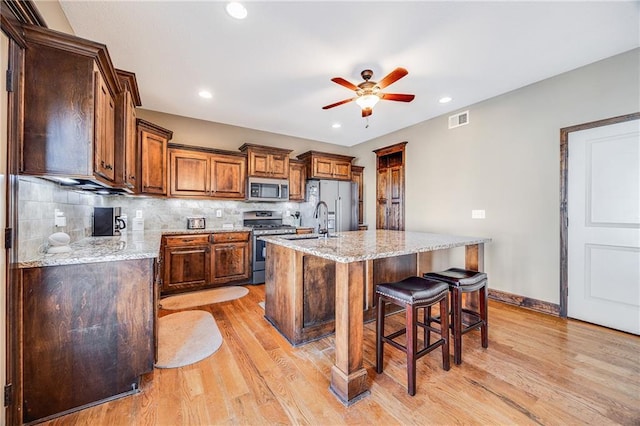 4000 S Buckner Tarsney Rd, Grain Valley, MO 64029 - kitchen with stainless steel appliances, a ceiling fan, a sink, light wood-style floors, and a kitchen bar