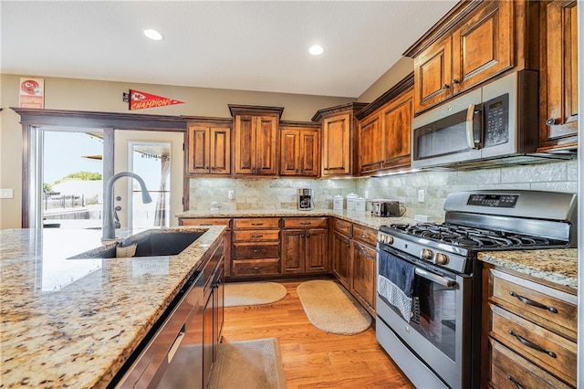 4000 S Buckner Tarsney Rd, Grain Valley, MO 64029 - kitchen featuring appliances with stainless steel finishes, a sink, light wood-style flooring, light stone countertops, and backsplash