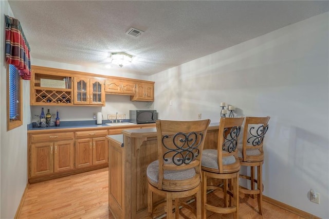 1407 SW Meyer Blvd, Blue Springs, MO 64015 - kitchen with black microwave, a breakfast bar, glass insert cabinets, a textured ceiling, and light wood-type flooring