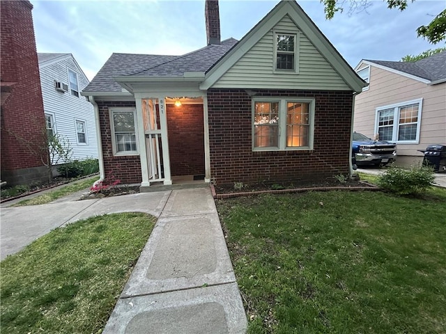 view of front of home featuring brick siding, a front yard, a chimney, and roof with shingles