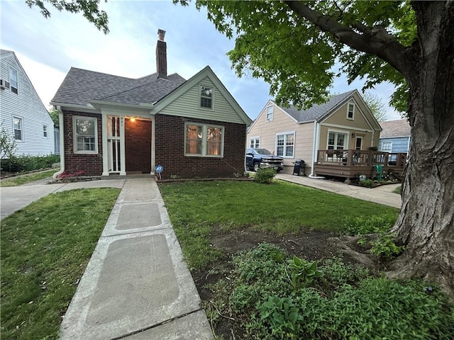 bungalow-style house with brick siding, a chimney, a front yard, and a deck