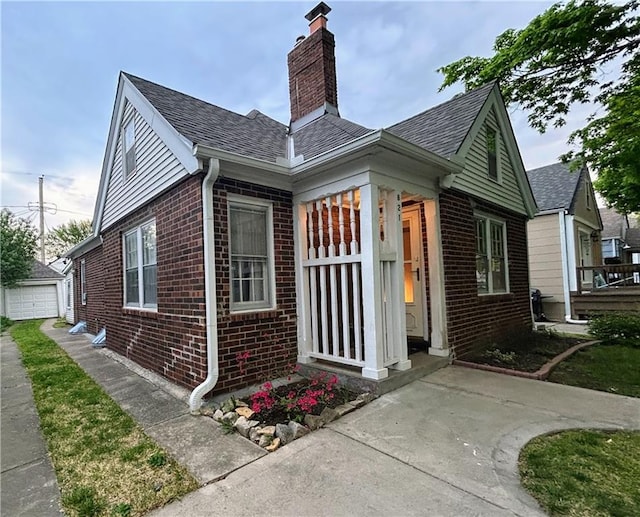 view of exterior entry with brick siding, a chimney, roof with shingles, and a garage