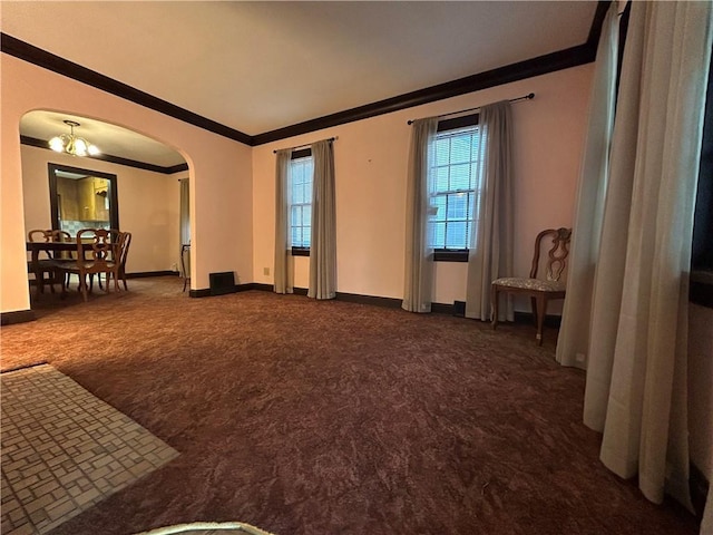 spare room featuring ornamental molding, arched walkways, dark carpet, baseboards, and a chandelier