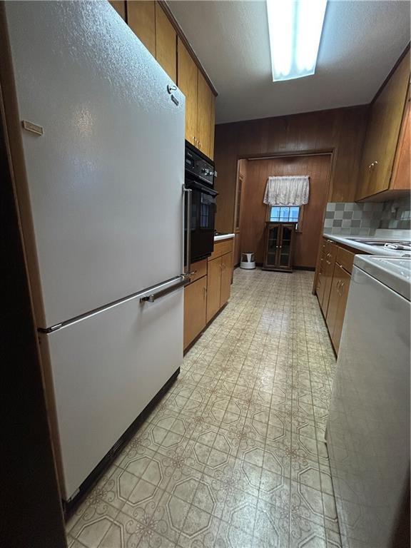 kitchen featuring freestanding refrigerator, oven, backsplash, and brown cabinets