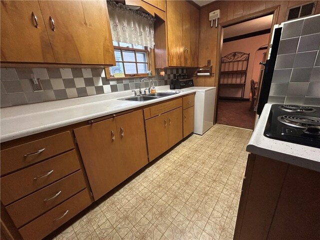 kitchen featuring washer / dryer, a sink, light countertops, tasteful backsplash, and brown cabinets