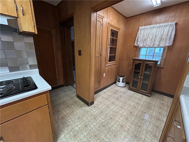 kitchen with brown cabinetry, light countertops, black electric cooktop, light floors, and wood walls