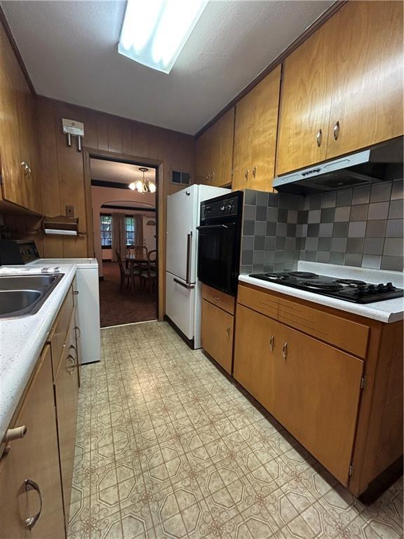kitchen with under cabinet range hood, black appliances, light countertops, a sink, and brown cabinetry