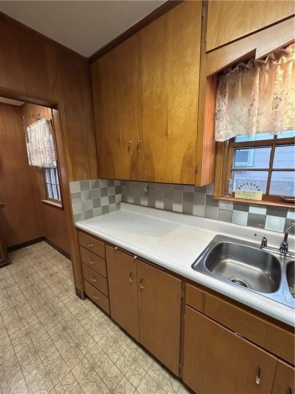 kitchen featuring a sink, light countertops, decorative backsplash, brown cabinets, and light flooring