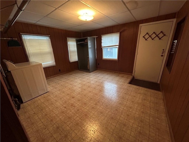 unfurnished bedroom featuring a paneled ceiling, wood walls, light flooring, and baseboards