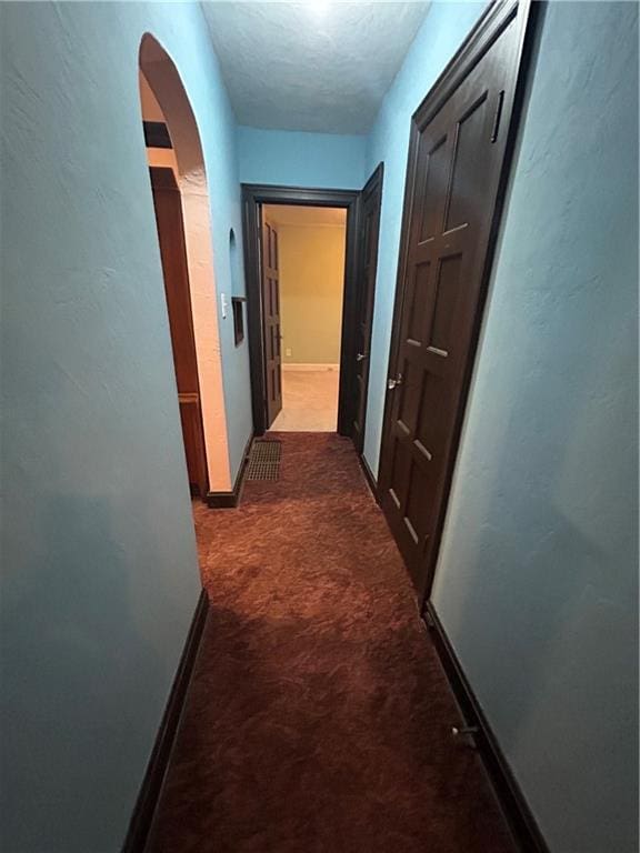 hall with arched walkways, carpet floors, baseboards, and a textured ceiling