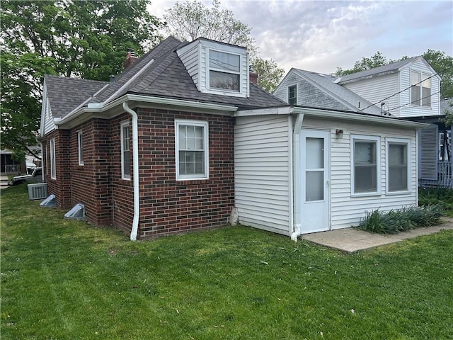 view of side of home featuring a yard, roof with shingles, and brick siding