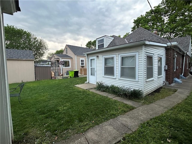 view of side of home with a yard and a shingled roof
