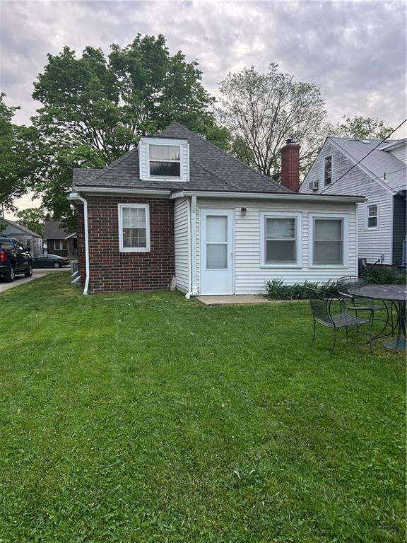 view of front of home with brick siding, a front yard, a shingled roof, and a chimney