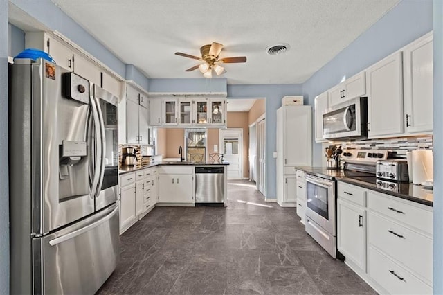 kitchen featuring stainless steel appliances, dark countertops, tasteful backsplash, a ceiling fan, and a textured ceiling