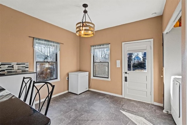 unfurnished dining area with a chandelier, washer / dryer, and baseboards