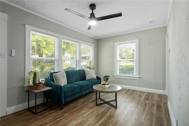 living area featuring wood finished floors, a ceiling fan, a textured ceiling, ornamental molding, and baseboards