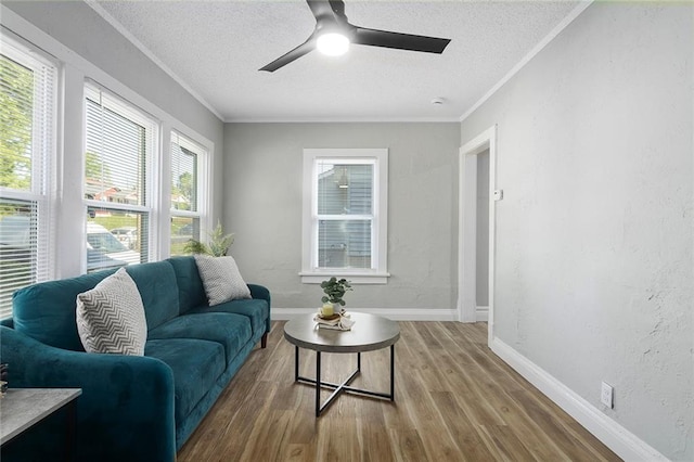 living area with a textured ceiling, ceiling fan, wood finished floors, crown molding, and baseboards