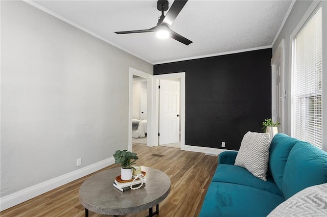 living area with wood finished floors, baseboards, a ceiling fan, and crown molding