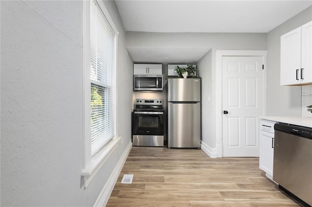 kitchen with stainless steel appliances, white cabinets, baseboards, light wood-style flooring, and light countertops