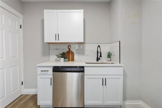 kitchen with stainless steel dishwasher, a sink, white cabinetry, baseboards, and light countertops