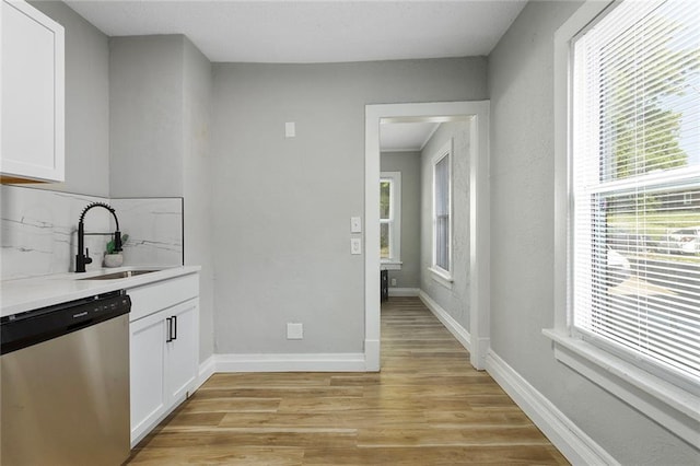 kitchen featuring dishwasher, a sink, light wood-style floors, white cabinets, and backsplash