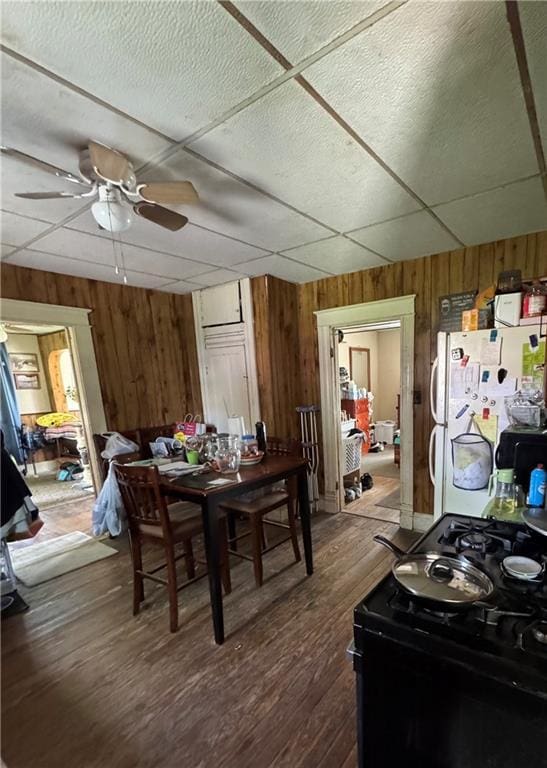 dining room with wood walls, ceiling fan, and dark wood-type flooring