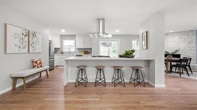 8741 Reeds Rd, Overland Park, KS 66207 - kitchen with wall chimney exhaust hood, a breakfast bar area, a sink, a peninsula, and white cabinetry