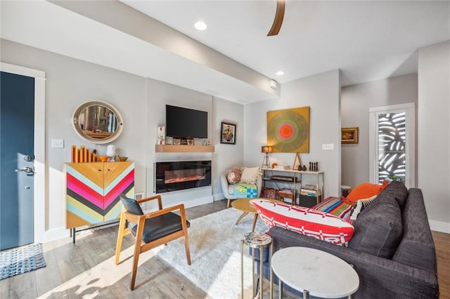 living area with wood finished floors, a glass covered fireplace, baseboards, recessed lighting, and ceiling fan