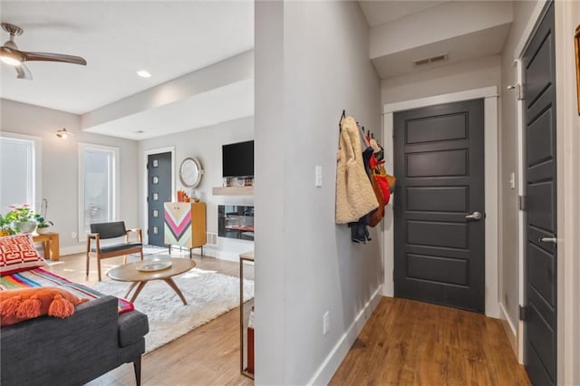 foyer entrance with wood finished floors, ceiling fan, baseboards, a glass covered fireplace, and recessed lighting