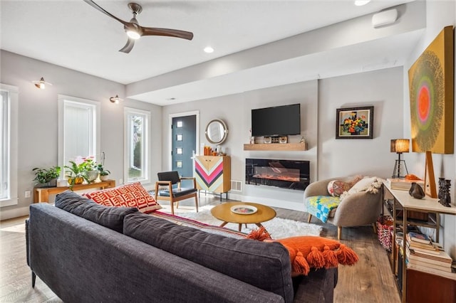 living area featuring ceiling fan, wood finished floors, healthy amount of natural light, a glass covered fireplace, and recessed lighting