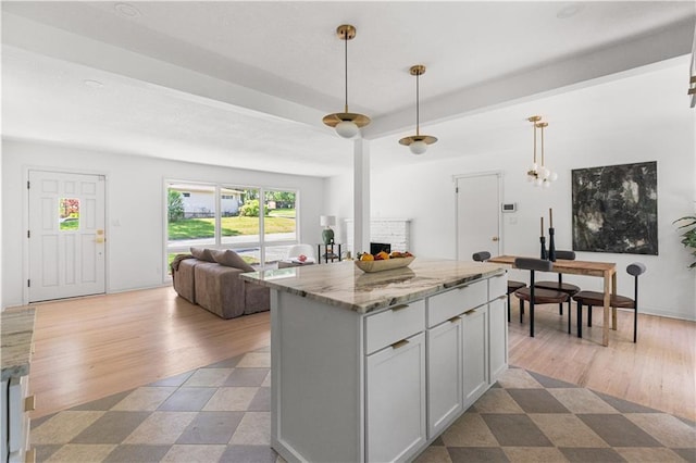 218 NW 43rd Ter, Kansas City, MO 64116 - kitchen featuring a brick fireplace, open floor plan, light stone countertops, a center island, and hanging light fixtures