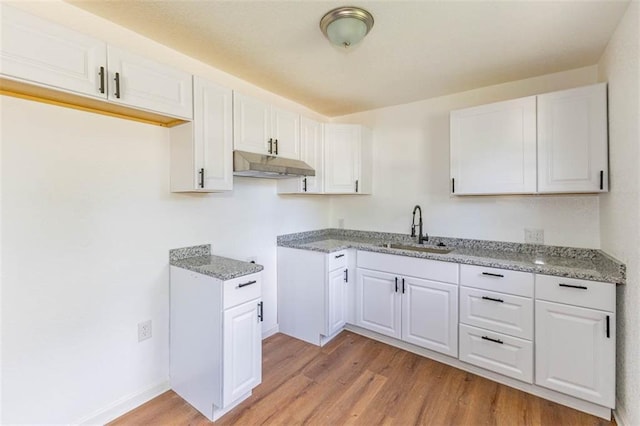 6021 E 151st Ter, Grandview, MO 64030 - kitchen with a sink, under cabinet range hood, light wood-style flooring, light stone counters, and white cabinetry
