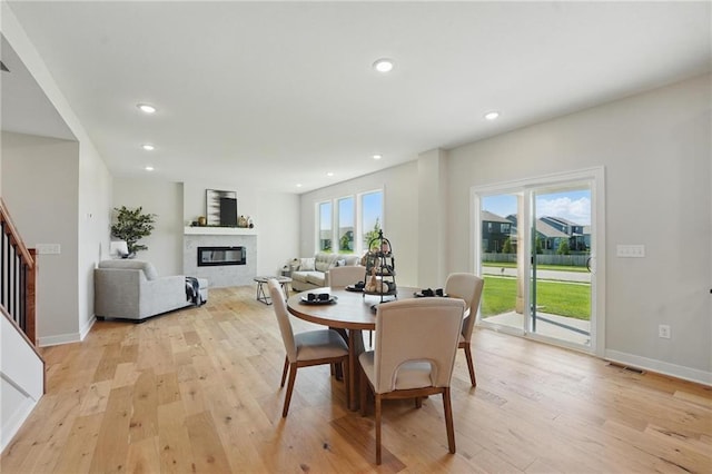 dining space with a glass covered fireplace, light wood finished floors, stairs, recessed lighting, and baseboards