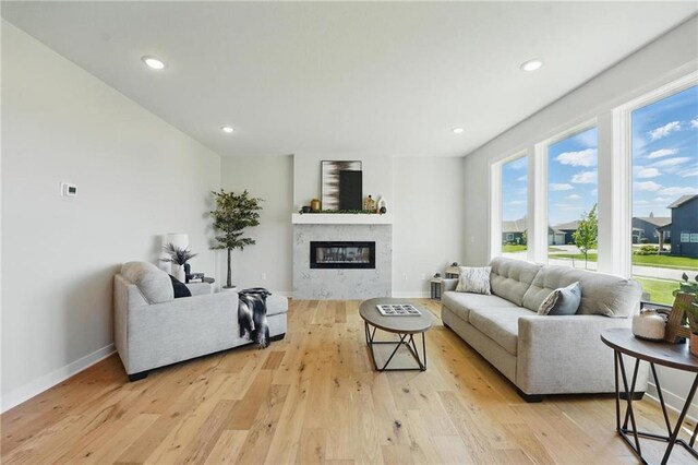 living area with a glass covered fireplace, light wood finished floors, baseboards, and recessed lighting