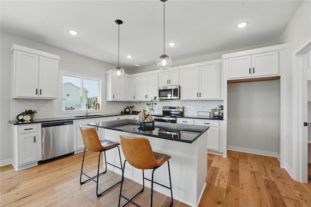kitchen featuring appliances with stainless steel finishes, a sink, dark countertops, white cabinets, and recessed lighting