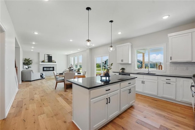 kitchen with a sink, dark countertops, a glass covered fireplace, decorative backsplash, and recessed lighting