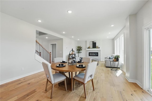 dining space with a glass covered fireplace, light wood-style floors, recessed lighting, baseboards, and stairway