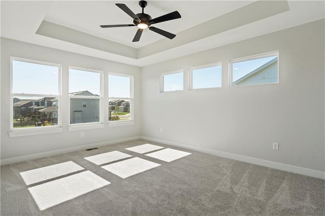spare room with a tray ceiling, carpet flooring, baseboards, and ceiling fan