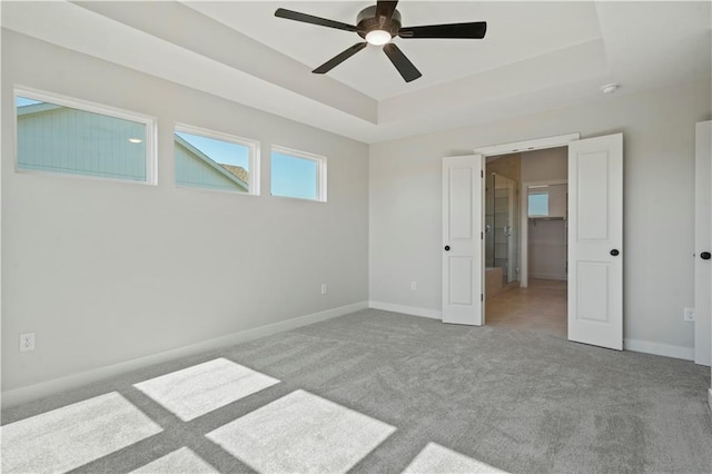 carpeted empty room with a tray ceiling, a ceiling fan, and baseboards