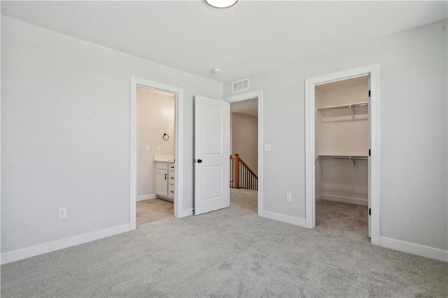 unfurnished bedroom with light colored carpet, a walk in closet, a closet, and baseboards