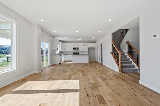 unfurnished living room featuring stairs, light wood finished floors, baseboards, and recessed lighting
