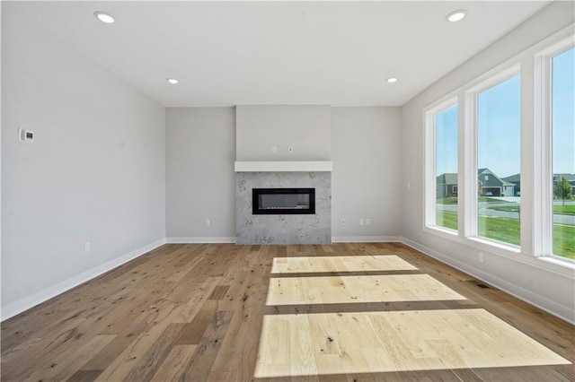 unfurnished living room featuring wood finished floors, baseboards, a glass covered fireplace, and recessed lighting