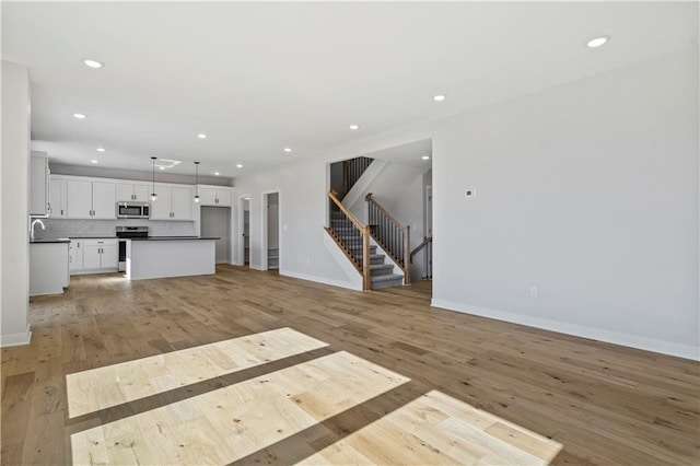 unfurnished living room featuring a sink, stairway, light wood-style floors, recessed lighting, and baseboards