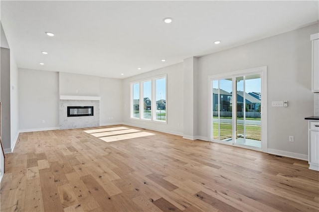 unfurnished living room featuring light wood-type flooring, recessed lighting, baseboards, and a premium fireplace