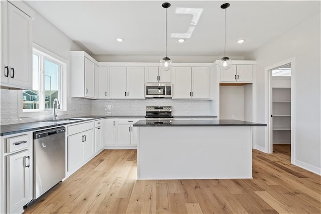 kitchen featuring stainless steel appliances, a sink, white cabinetry, dark countertops, and light wood finished floors